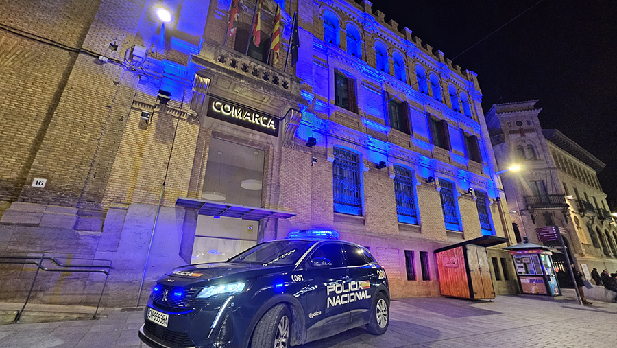 Coche de Policía Nacional frente a edificio iluminado de color azul. 